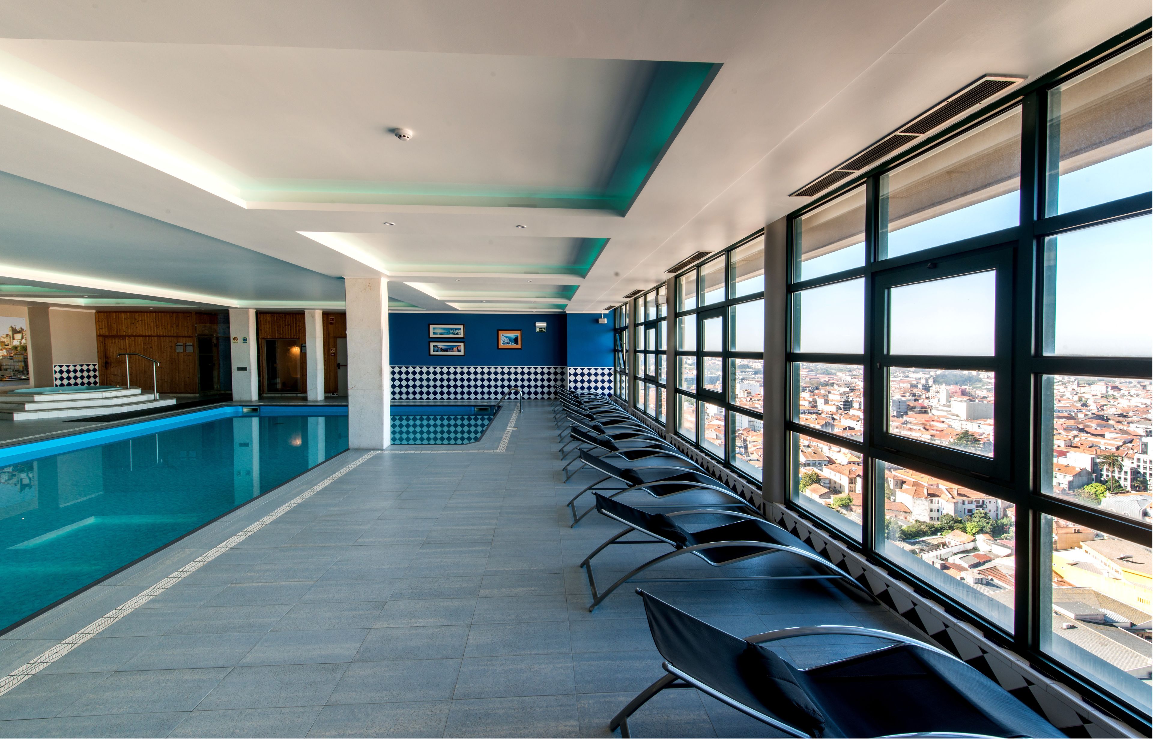 Ein langer Korridor mit einem Pool an einer Seite und einer Reihe von Stühlen, die auf ein großes Fenster mit Blick auf die Stadt ausgerichtet sind.