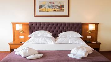 A neatly made bed with a tufted headboard, white pillows, and a purple blanket. There are two bedside tables with lamps and a framed artwork above the bed.