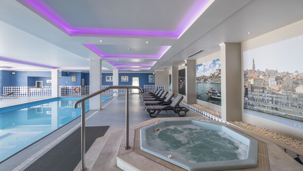 A modern indoor pool area with a hot tub, lounge chairs, and a city view. -  Vila Gale Porto Centro Hotel (Porto)