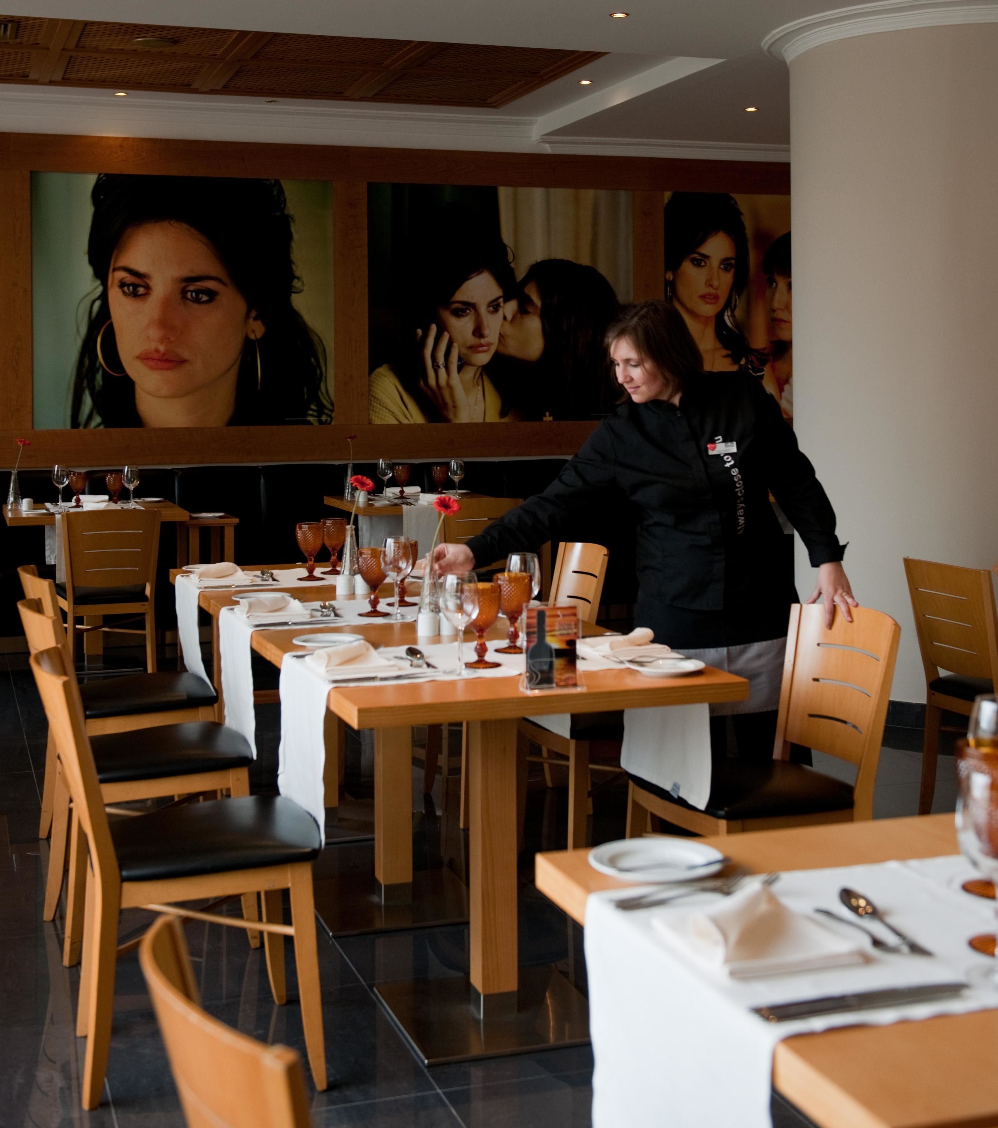A restaurant with wooden tables and chairs, each set with plates, cutlery, and glasses.
