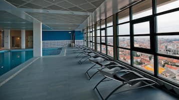 Un espace piscine avec vue sur la ville, des bancs et un sol carrelé.