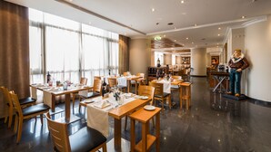 A spacious restaurant with multiple dining tables and chairs, large windows, and a statue of a man. -  Vila Gale Porto Centro Hotel (Porto)