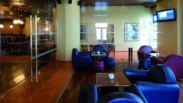 A modern lounge area with glass partitions, comfortable seating, and a television on the wall.