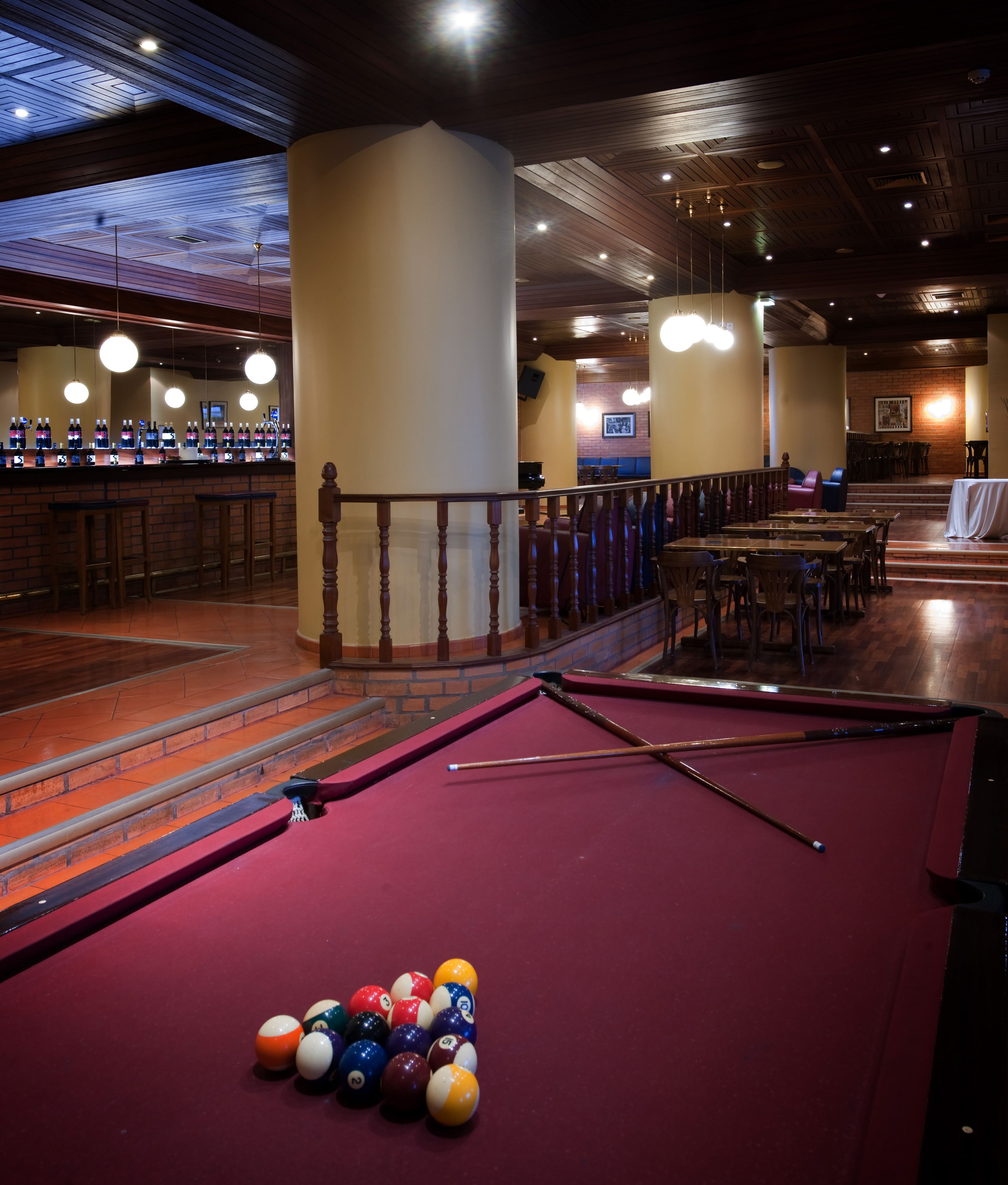 Une table de billard avec des billes, des chaises en bois et un coin bar avec des bouteilles.