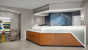 Un moderno mostrador de recepción con acabado de madera y superficie blanca, ubicado en una habitación con piso de tonos claros y un cuadro abstracto de gran tamaño en la pared.