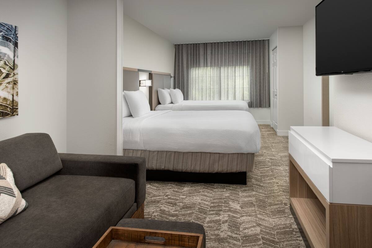 A hotel room with two beds, a sofa, a TV, and a painting on the wall.