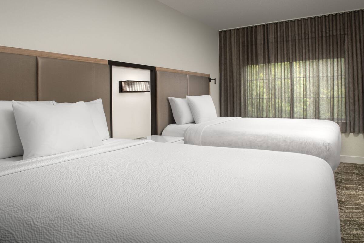A hotel room with two beds, a headboard, a window with curtains, and a carpeted floor.