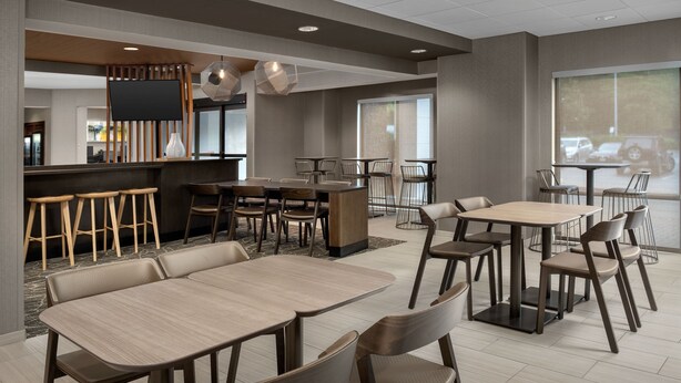 Un restaurante moderno con varias zonas de estar, incluidas cabinas y mesas, y un bar con taburetes.