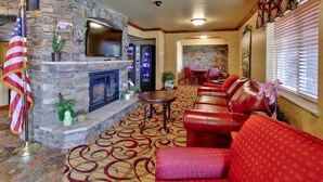 A living room with a stone fireplace, red leather sofas, a flat-screen TV, and an American flag. - MCM Elegante Suites (Colorado Springs)