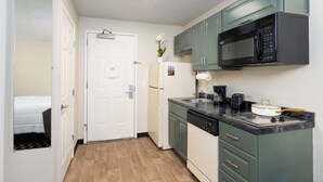 A compact kitchen with a microwave, stove, and sink. - MCM Elegante Suites (Colorado Springs)