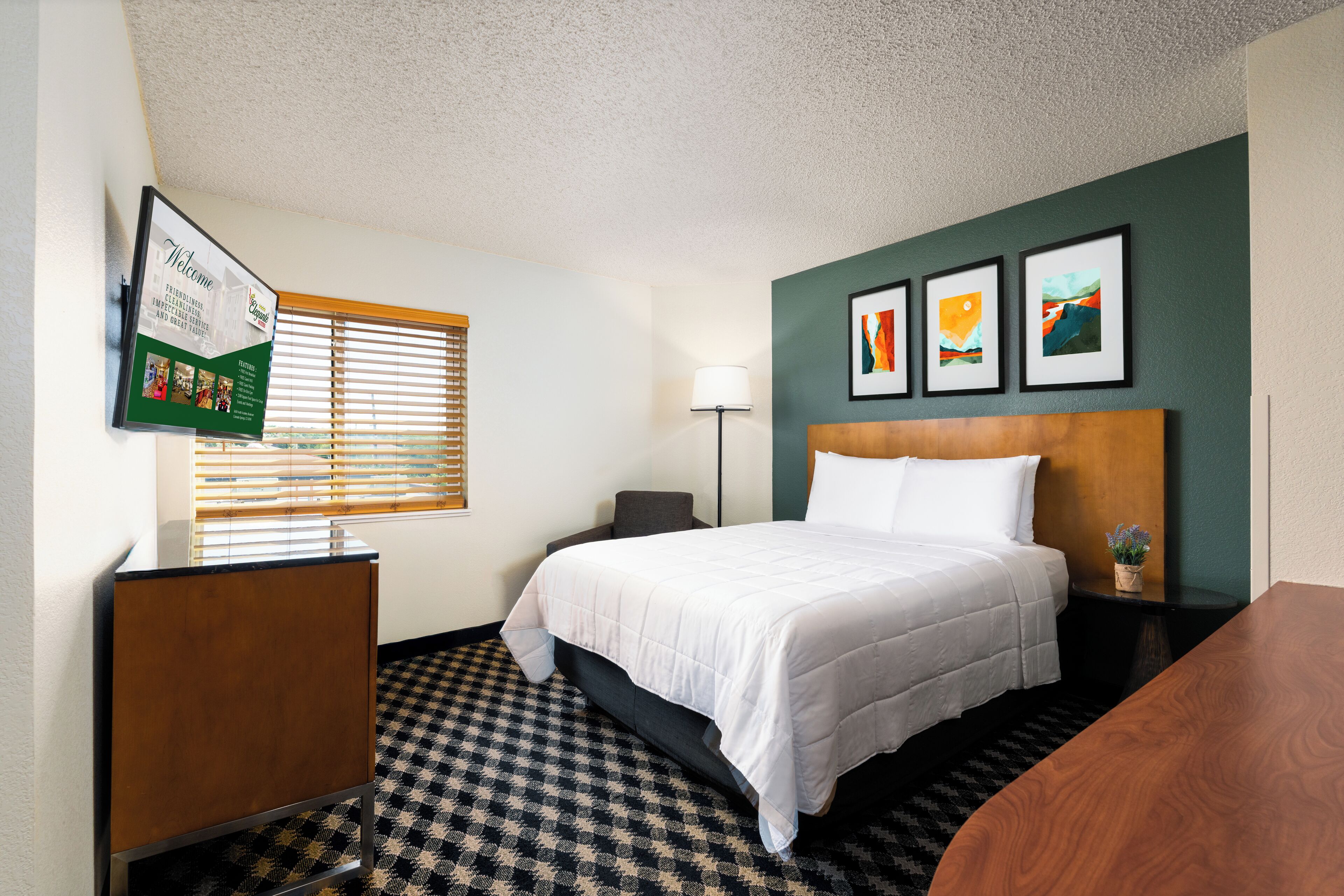 Hotelkamer met een bed, bureau, lamp en een aan de muur bevestigde televisie waarop een welkomstboodschap staat.