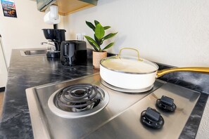 A kitchen with a stove, a pot on the stove, a coffee maker, a toaster, and a potted plant. - MCM Elegante Suites (Colorado Springs)