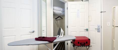 A compact room with a foldable ironing board, a red suitcase, and a mirror on the wall.