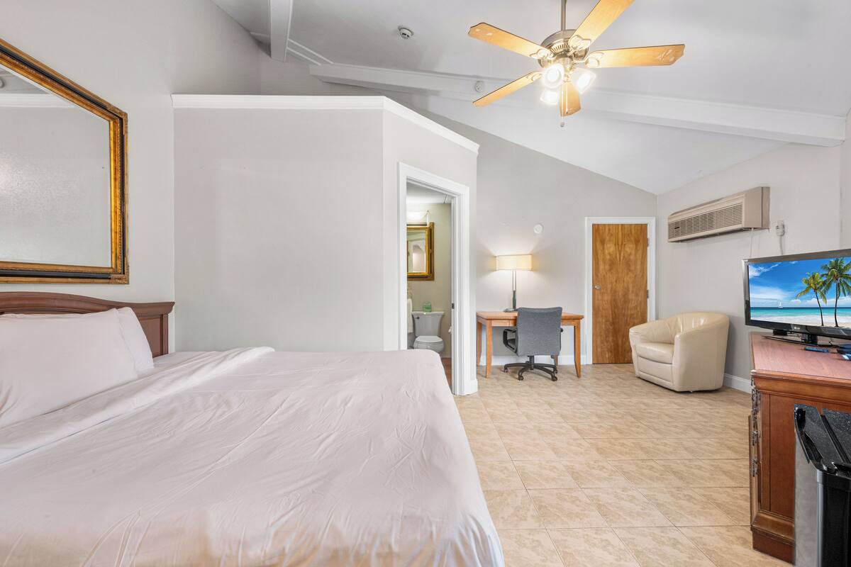 Ein Hotelzimmer mit Bett, Schreibtisch, Stuhl, Fernseher und Deckenventilator.