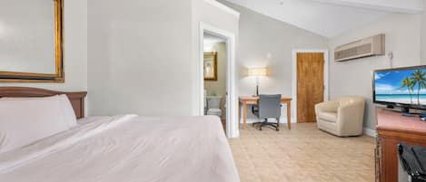 Habitación de hotel con cama, escritorio, silla, televisor y ventilador de techo.