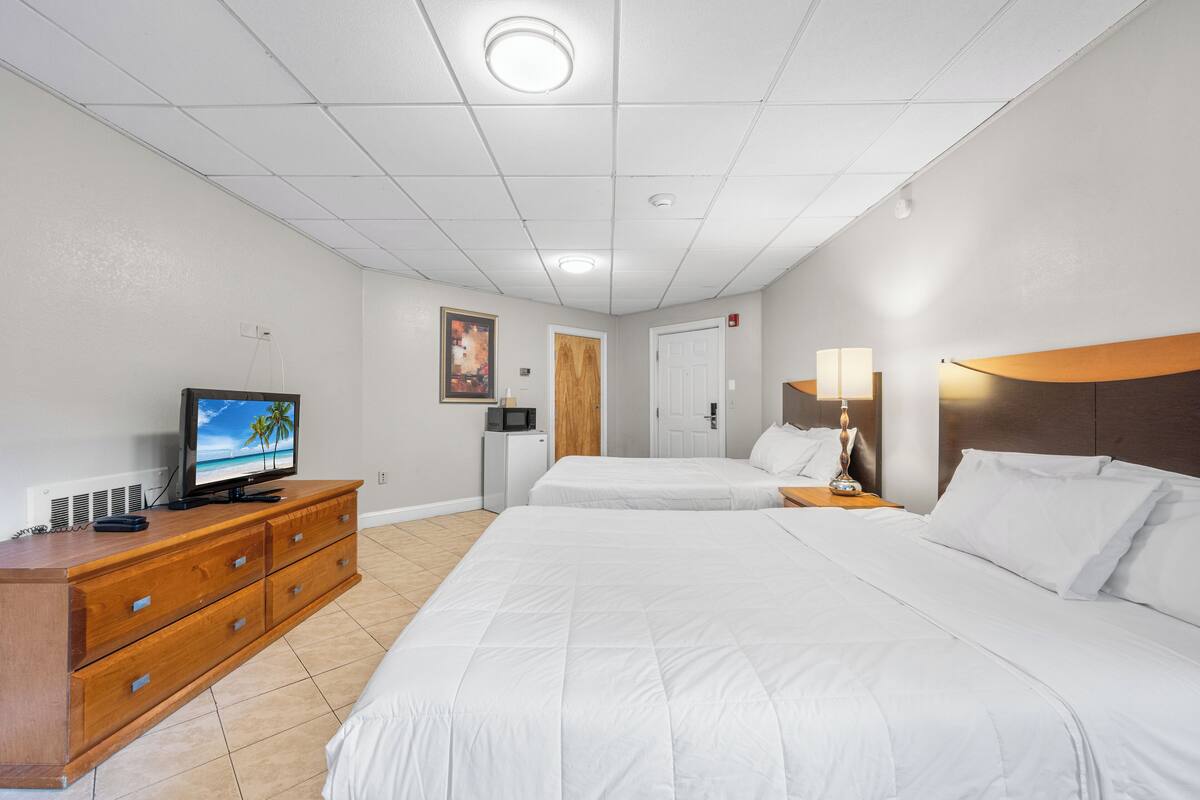Ein Hotelzimmer mit zwei Betten, einem Fernseher auf einer Kommode, einer Mikrowelle und einer Tür mit einem Holzpaneel.