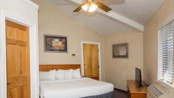 Ein Hotelzimmer mit einem Bett, einem Deckenventilator, einem Schreibtisch mit Computer und einem Fenster mit Jalousien.