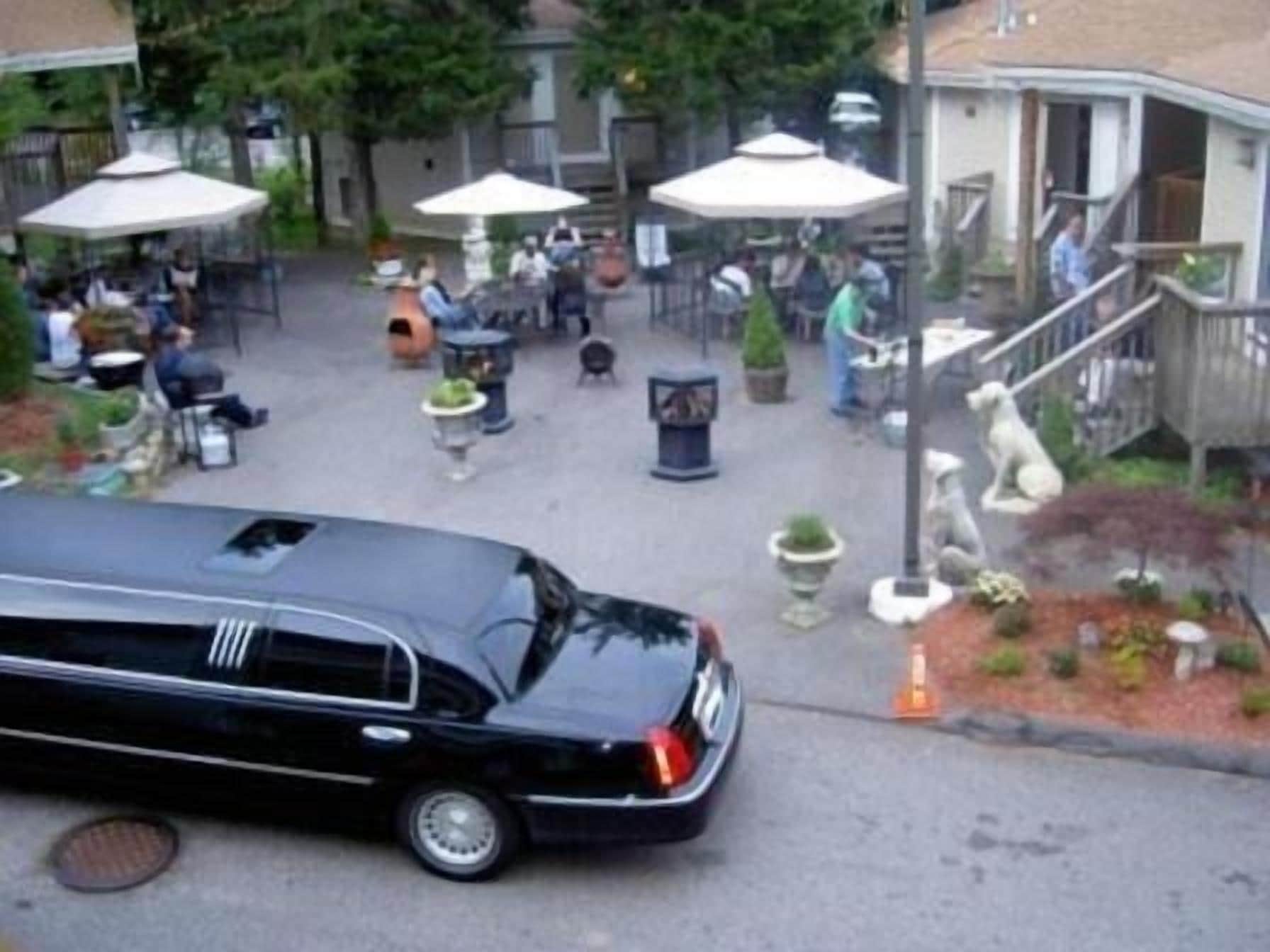 A black car parked in front of a building with outdoor seating and a statue.