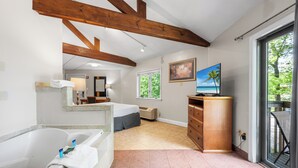 Ein Schlafzimmer mit großem Fenster, Holzboden, Bett, Schreibtisch und Blick ins Freie.