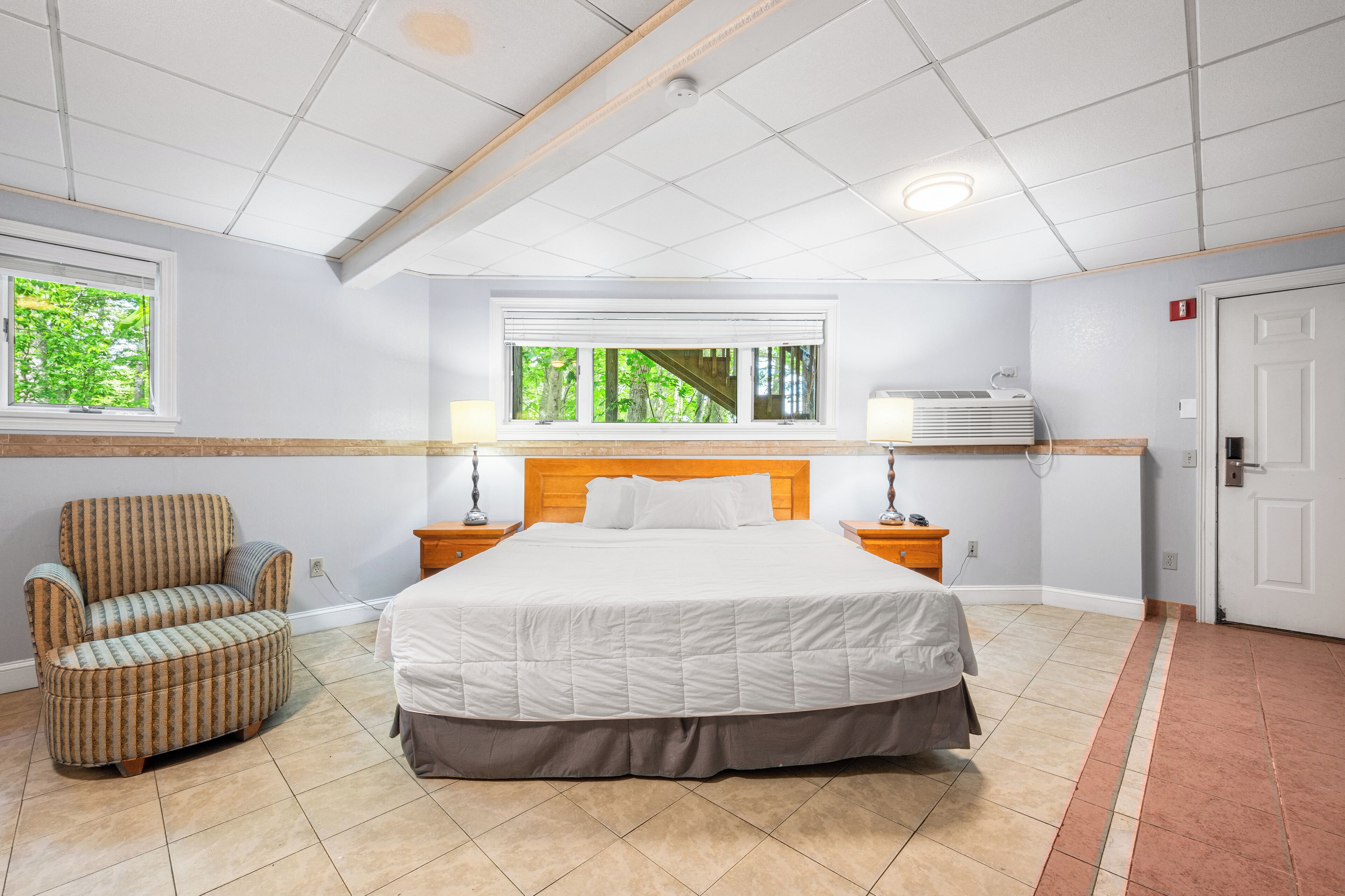 A bedroom with a large bed, a chair, a window, and a ceiling fan.