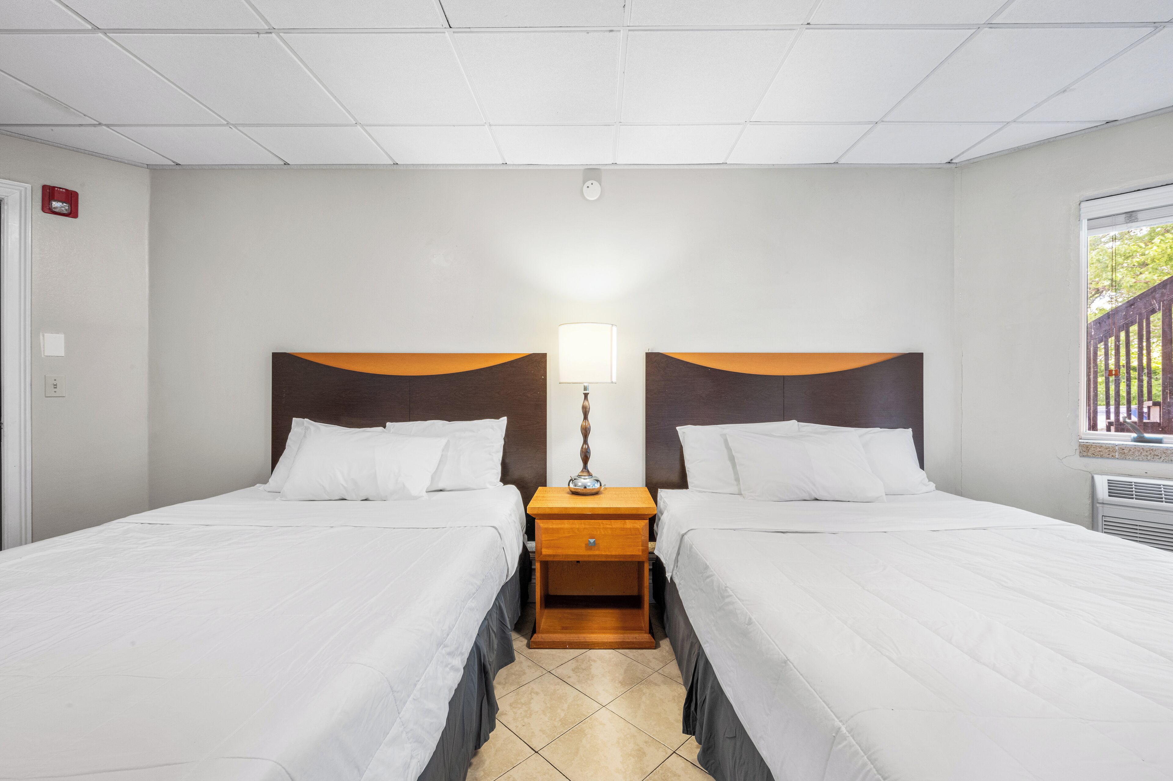 Une chambre d’hôtel avec deux lits simples, une table de chevet avec une lampe et une fenêtre donnant sur un paysage verdoyant.