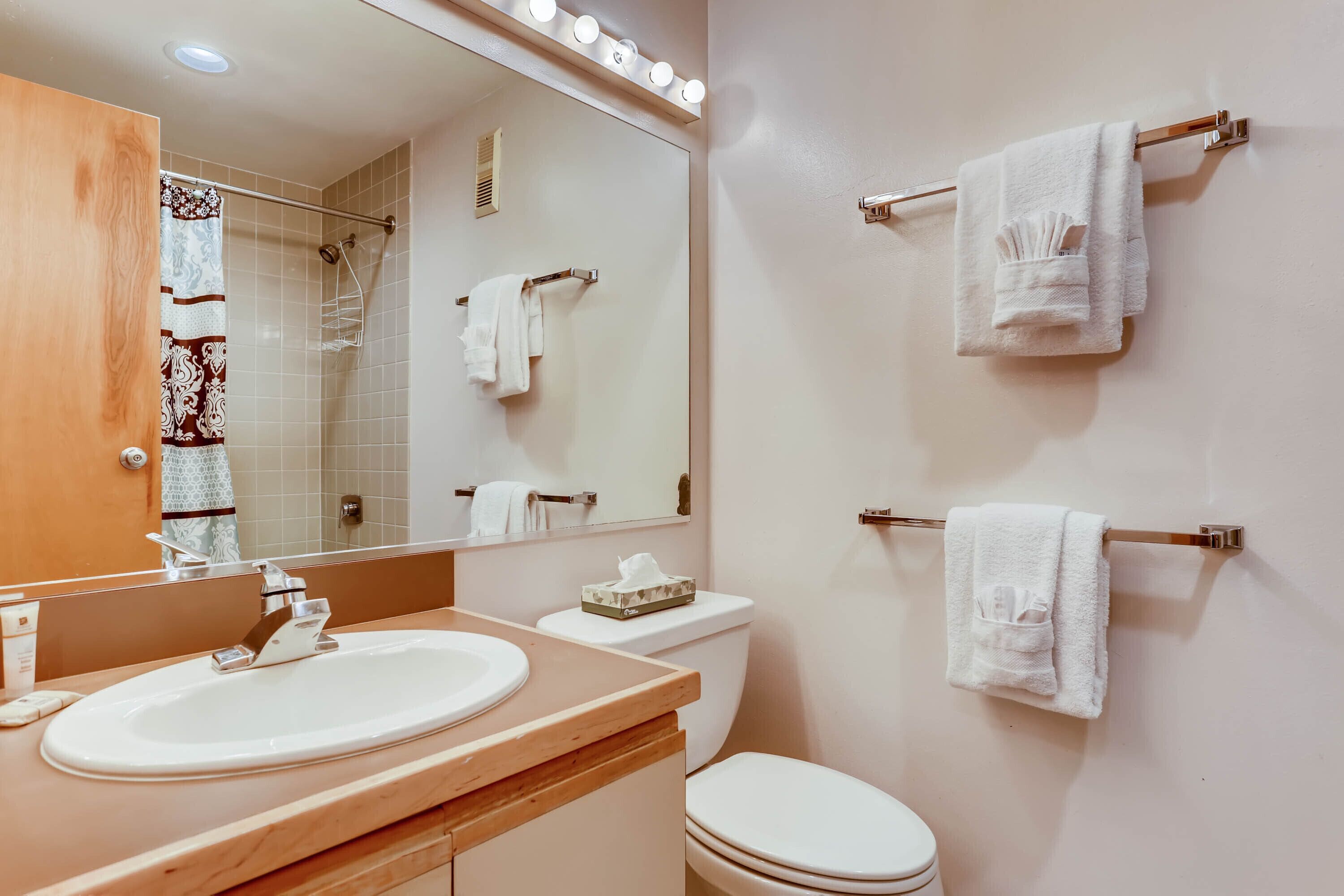 A bathroom with a wooden vanity, a white sink, a toilet, and a mirror with lights.