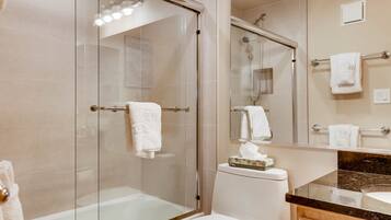 Een moderne badkamer met een douchecabine van glas, een wit toilet en een marmeren aanrechtblad.