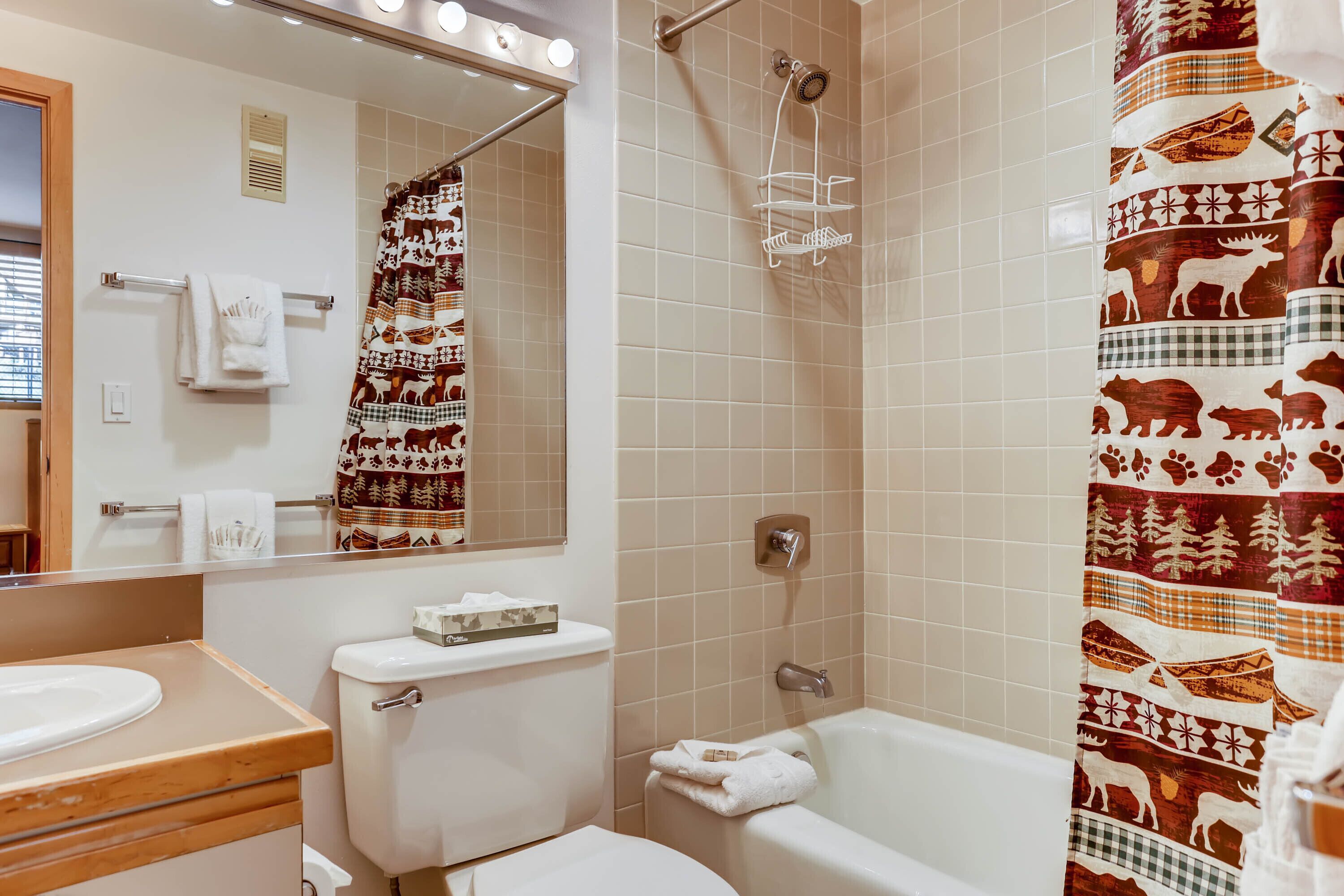 A bathroom with a toilet, sink, and bathtub. There is a shower curtain with animal prints.