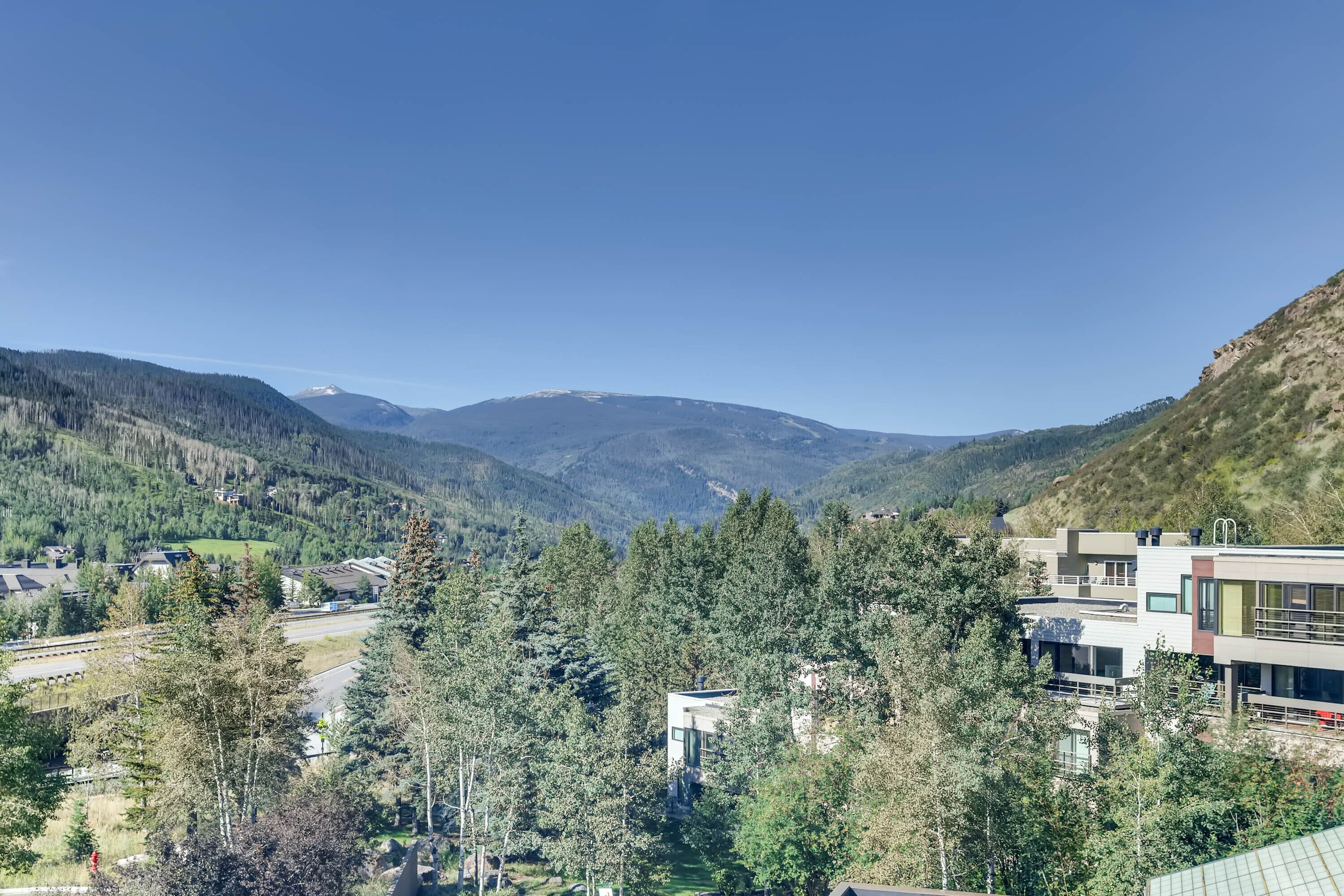 A modern building with a flat roof and large windows, surrounded by dense forest and mountains in the background.