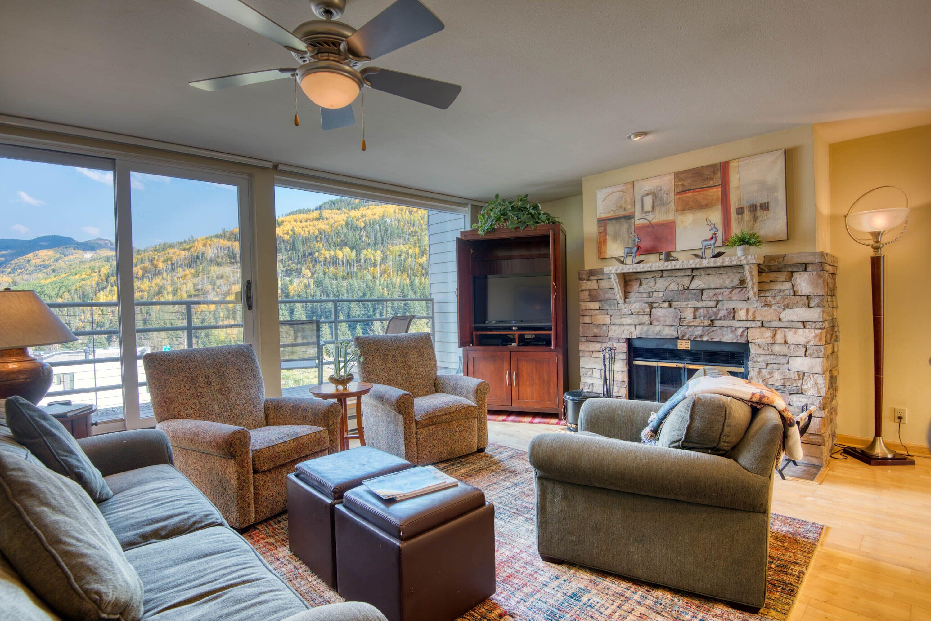 A spacious living room with a stone fireplace, comfortable seating, and a large window overlooking a scenic mountain view.