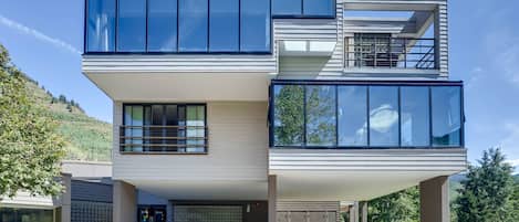 A modern two-story house with large windows, a flat roof, and a landscaped front yard.