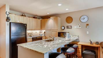 A kitchen with a central island, wooden cabinets, a black refrigerator, a sink, and a clock on the wall.