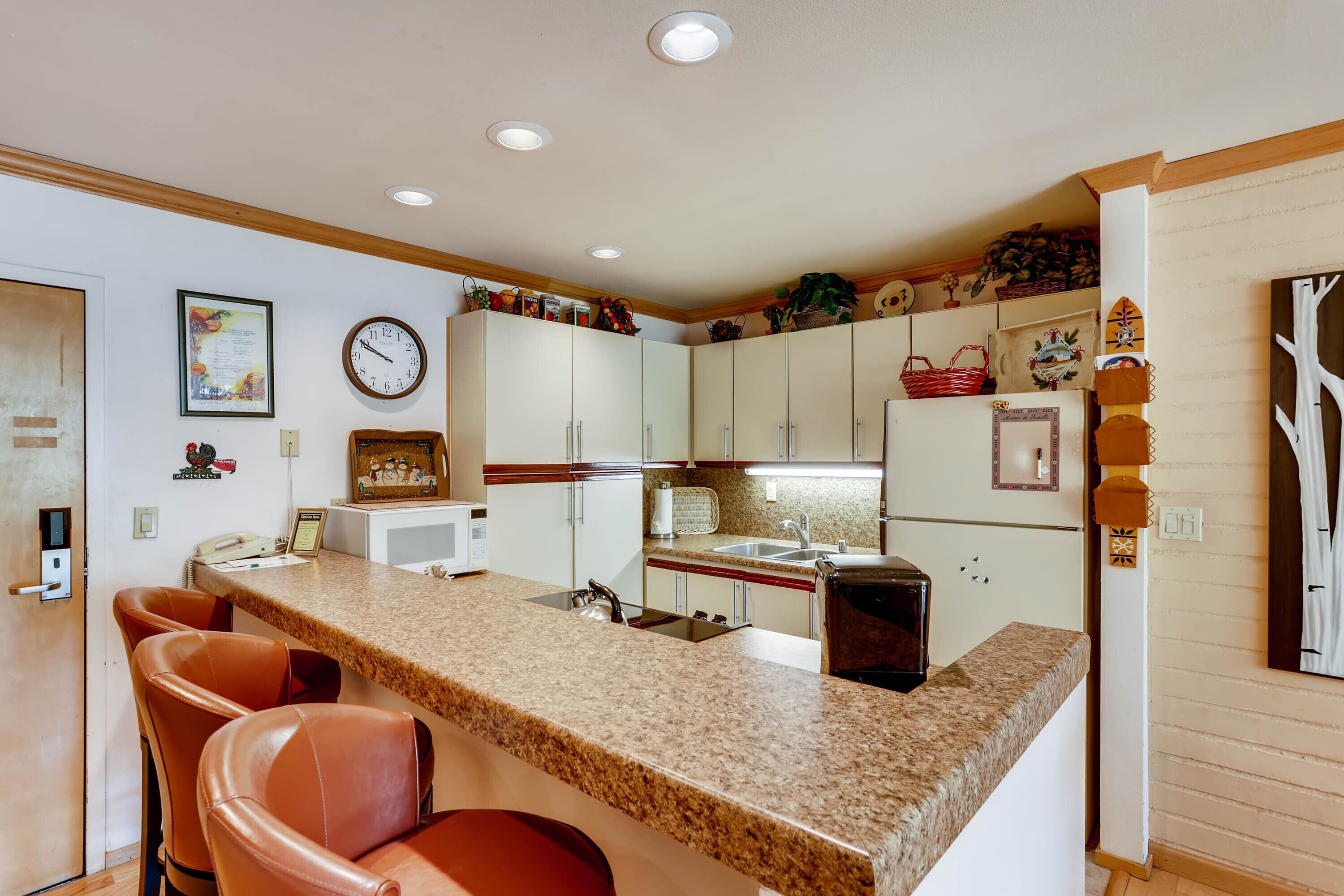 A kitchen with granite countertops, white cabinets, a refrigerator, and a clock on the wall.
