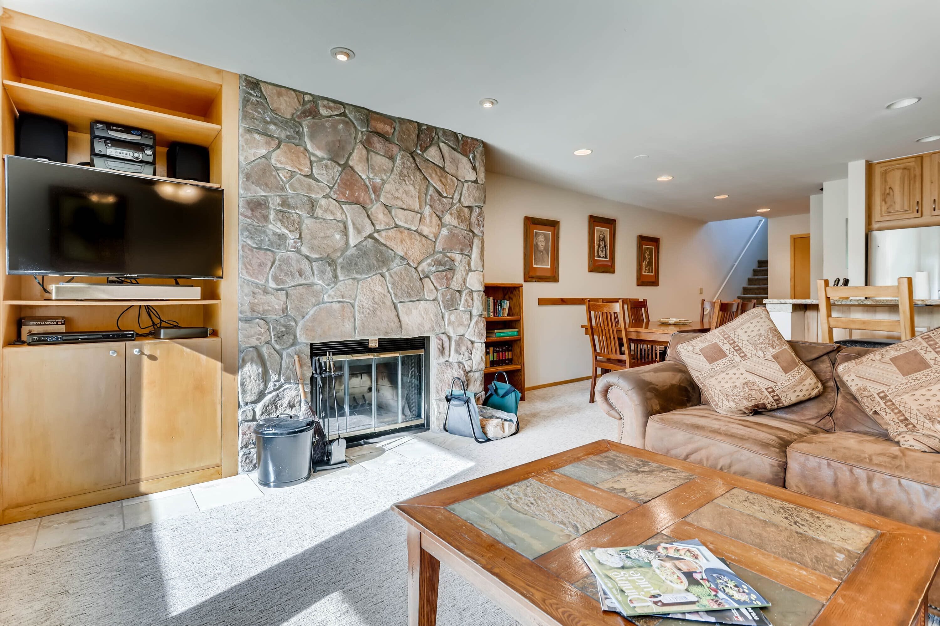 A spacious living room with a stone fireplace, wooden shelving with electronic devices, a comfortable sofa, and a coffee table.