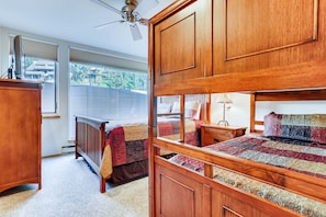 A bedroom with a bunk bed, a wooden dresser, a desk, and a window with blinds.