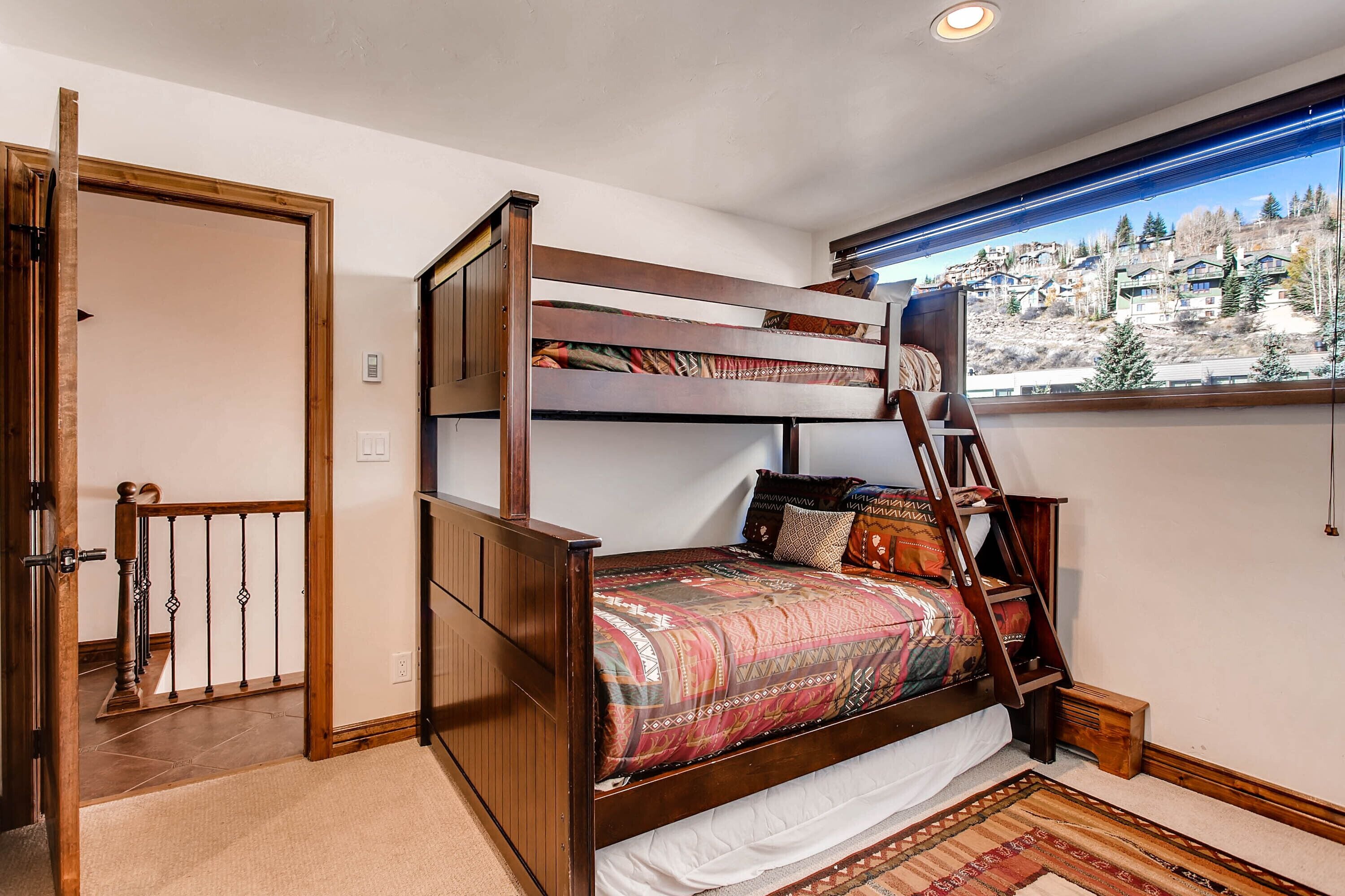 A bunk bed with a ladder, a window with a view of a mountainous landscape, and a wooden door.