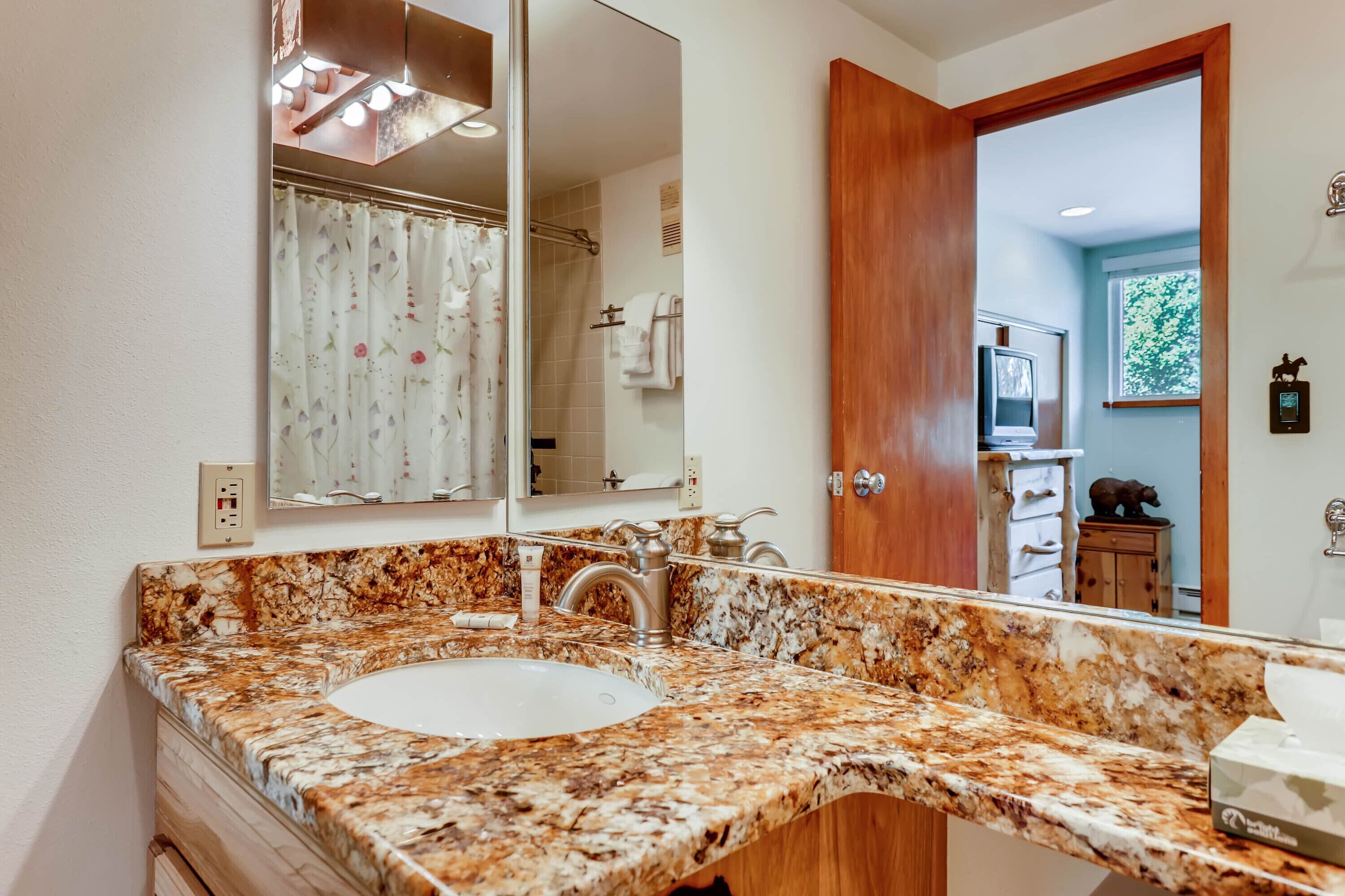 A bathroom with a marble sink, a large mirror, and a shower with a floral curtain.