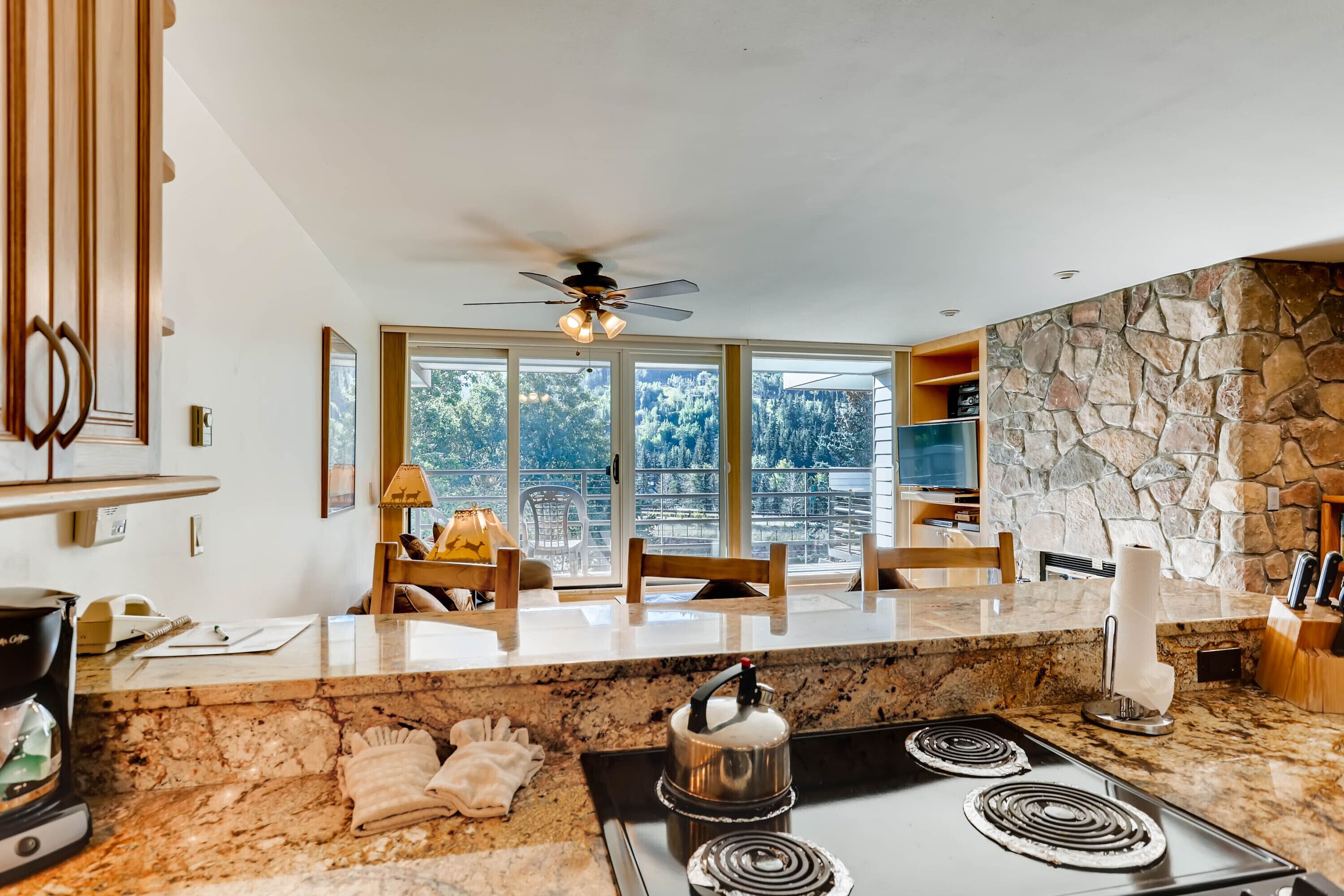 A modern kitchen with a stone accent wall, a large window with a view of trees, and a ceiling fan.