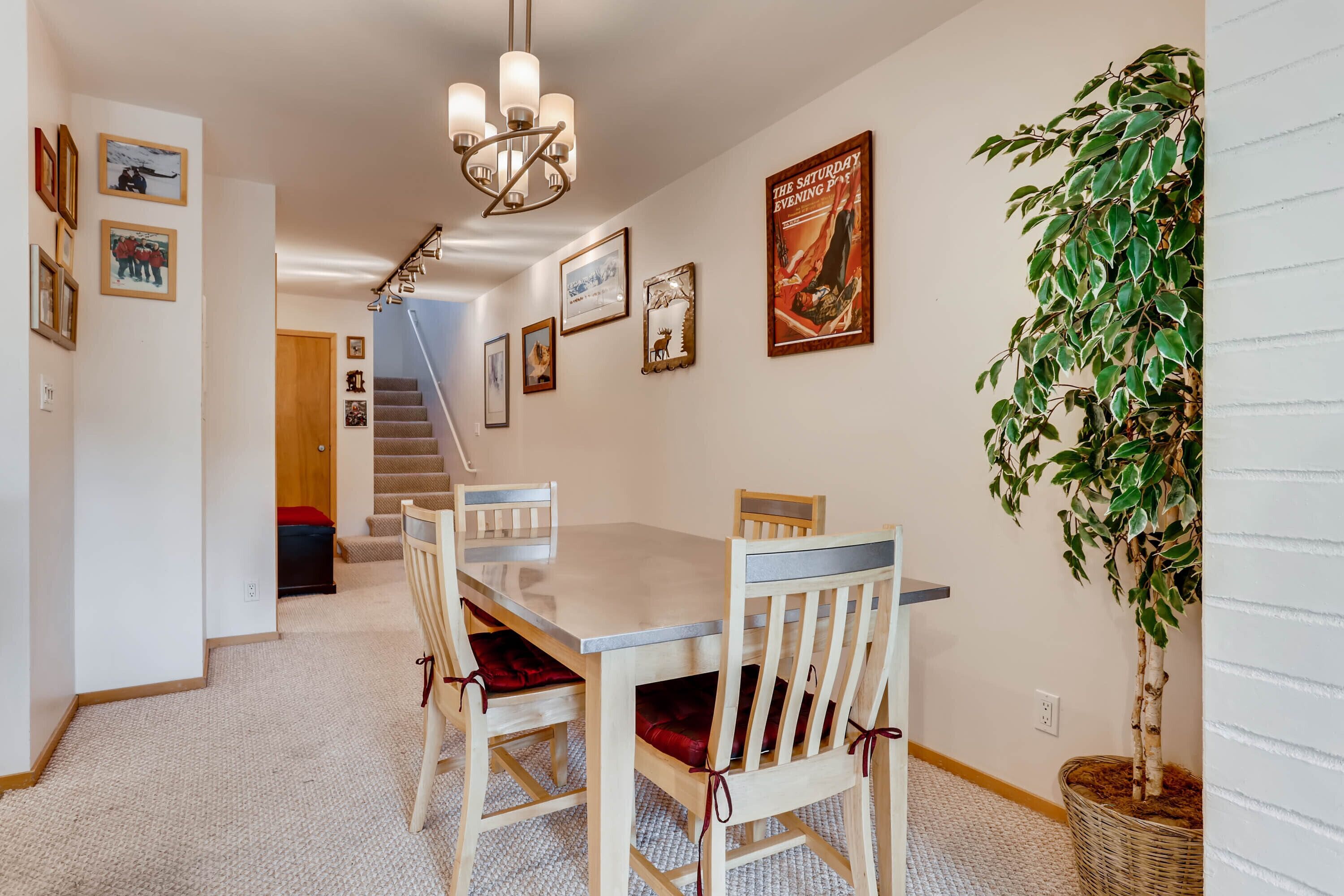 Un coin repas avec une table et des chaises en bois, un lustre, des tableaux encadrés aux murs et un escalier menant à l’étage.