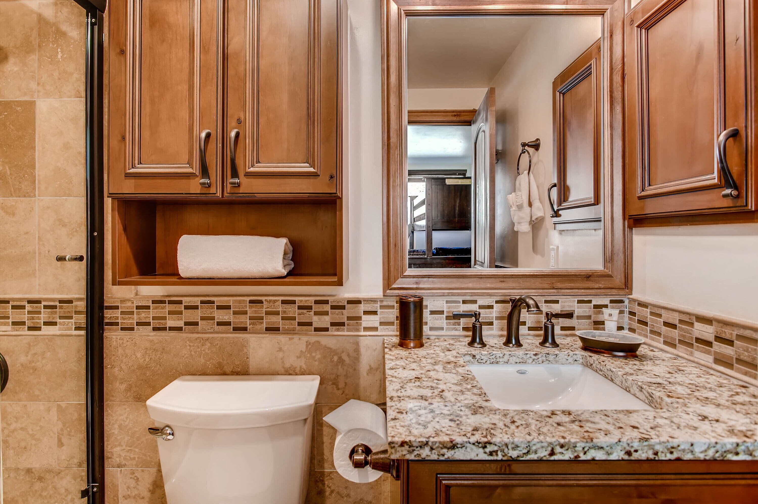 A bathroom with wooden cabinets, a marble countertop, a sink, and a toilet.