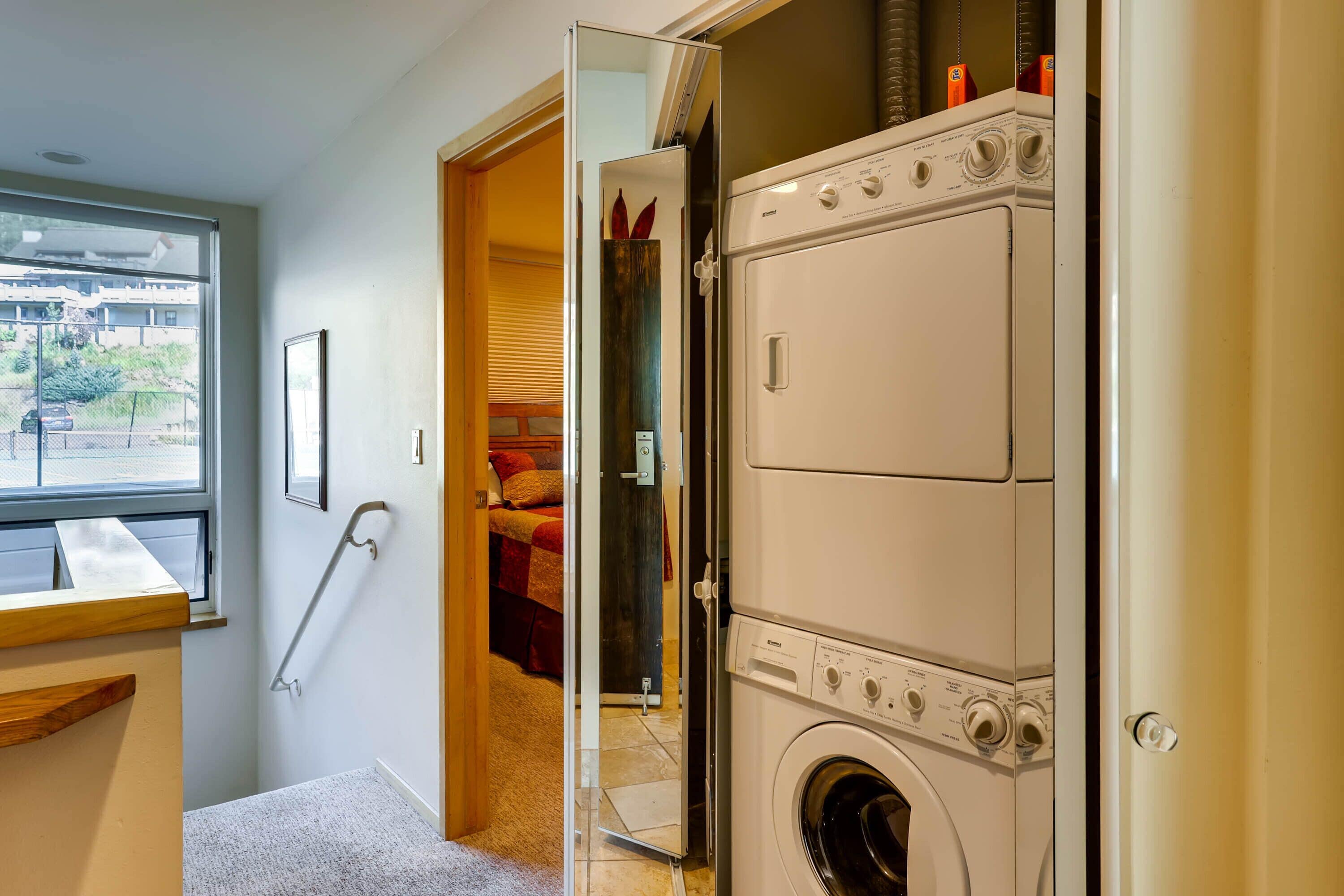 Un lavadero con lavadoras y secadoras apiladas, una ventana que ofrece vistas al exterior y una puerta que da a un dormitorio.