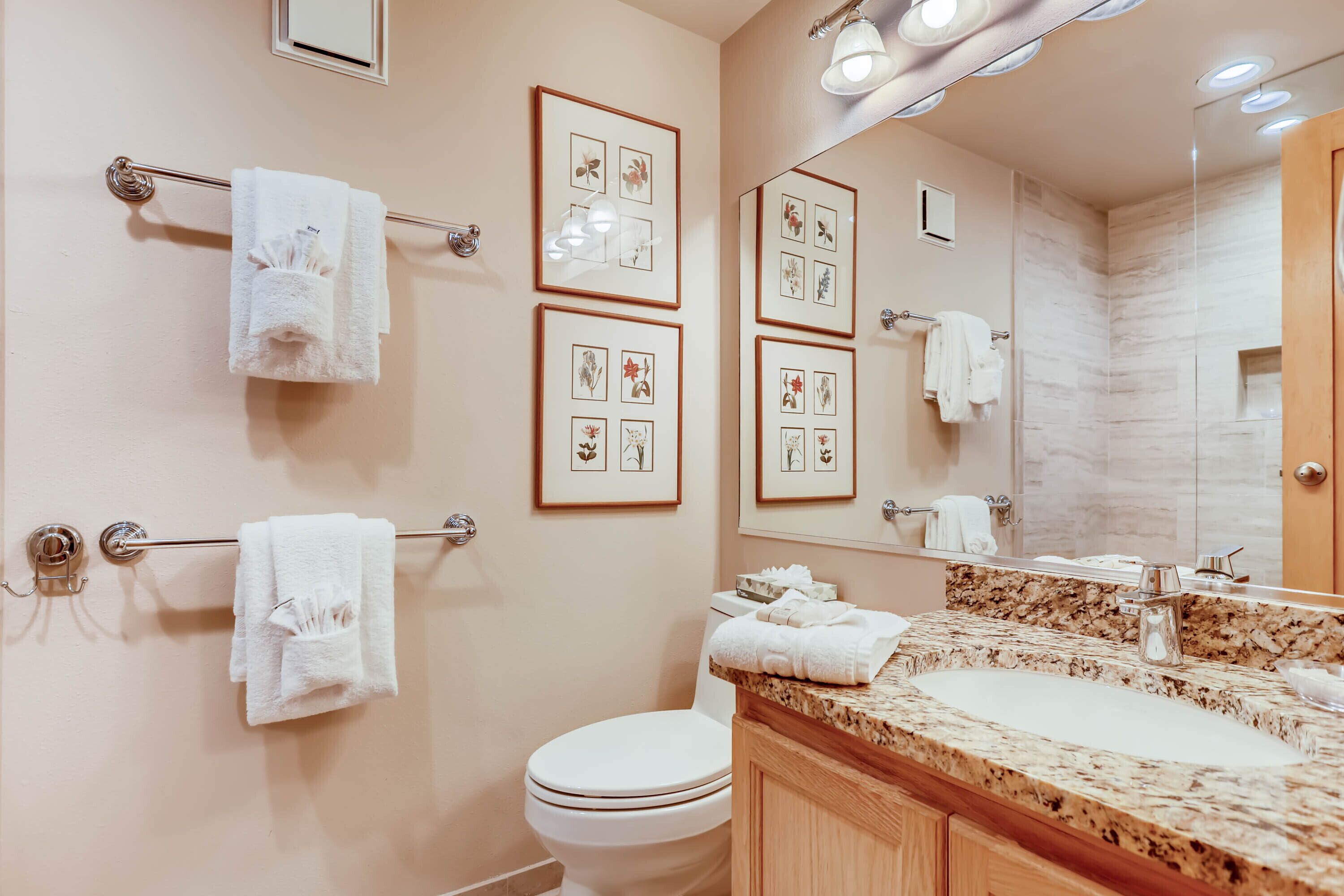 A bathroom with a marble sink, framed pictures on the wall, and multiple towels hanging on towel bars.
