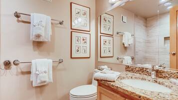 A bathroom with a marble sink, framed pictures on the wall, and multiple towels hanging on towel bars.