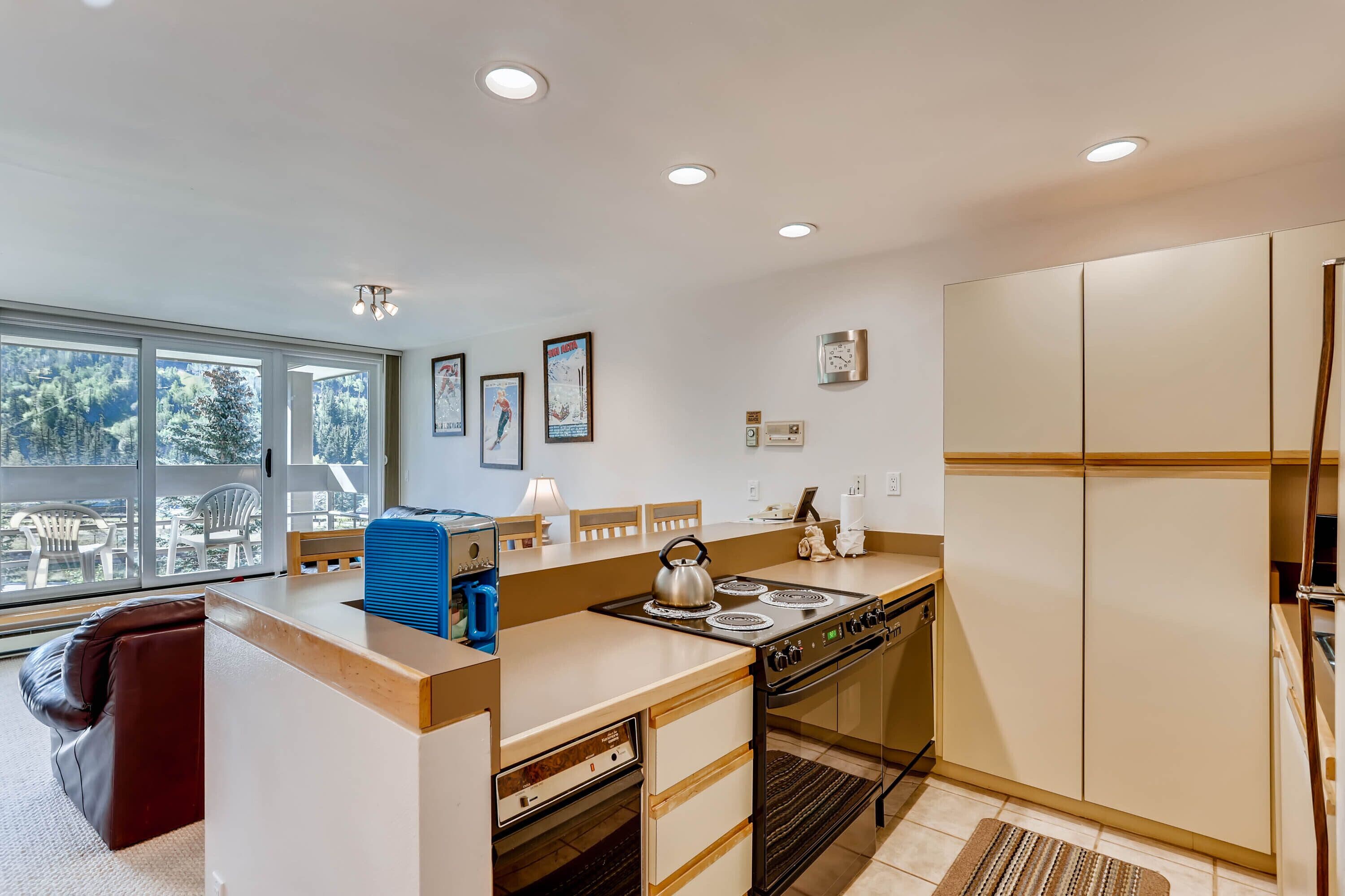 A modern kitchen with a central island, built-in oven, and large windows offering a view of the outdoors.