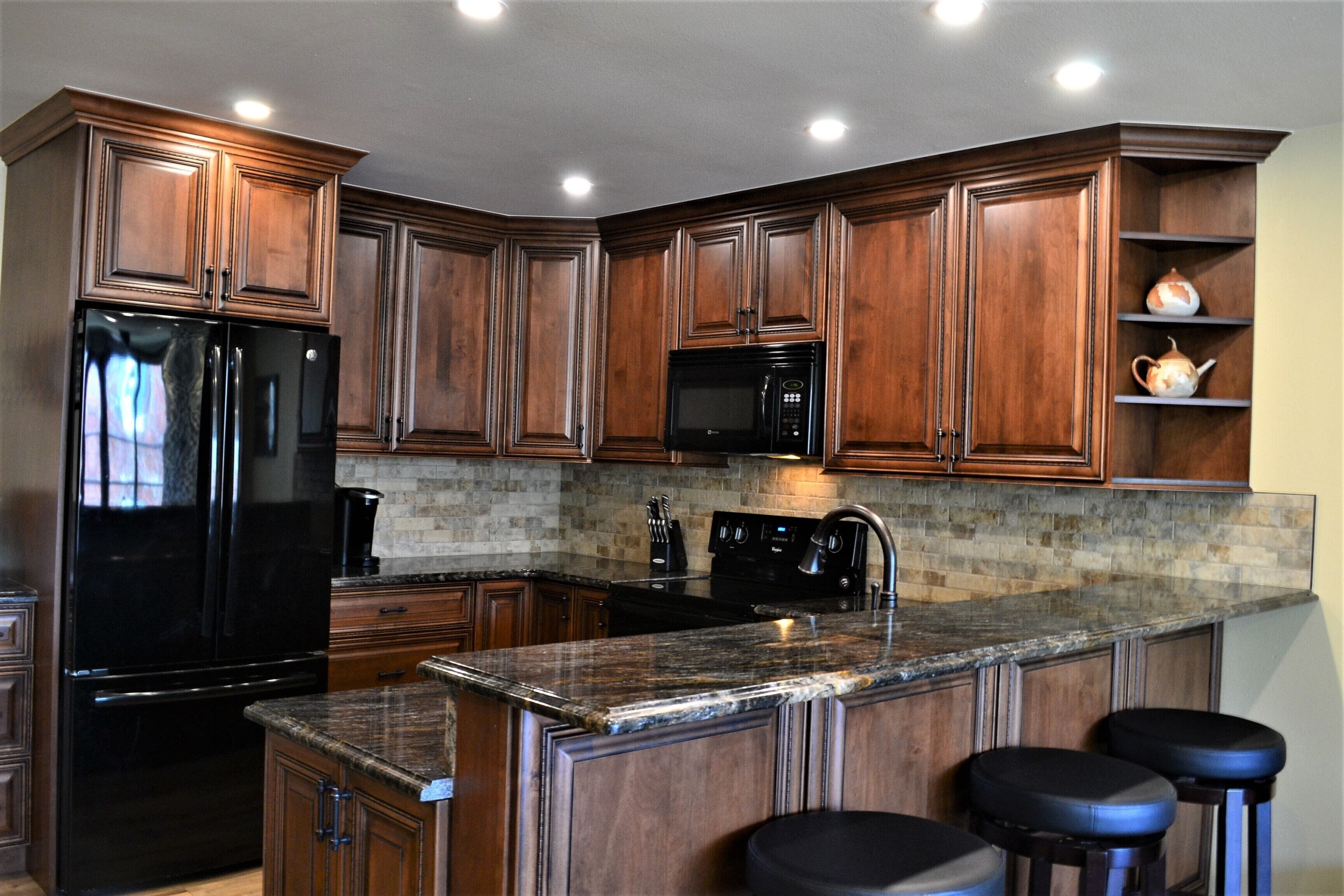 A kitchen with wooden cabinets, a black refrigerator, a microwave, and a granite countertop.