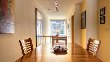 Une salle à manger avec une table en bois, quatre chaises et un bol de biscuits. Il y a une fenêtre donnant sur des arbres et une porte menant à une autre pièce.