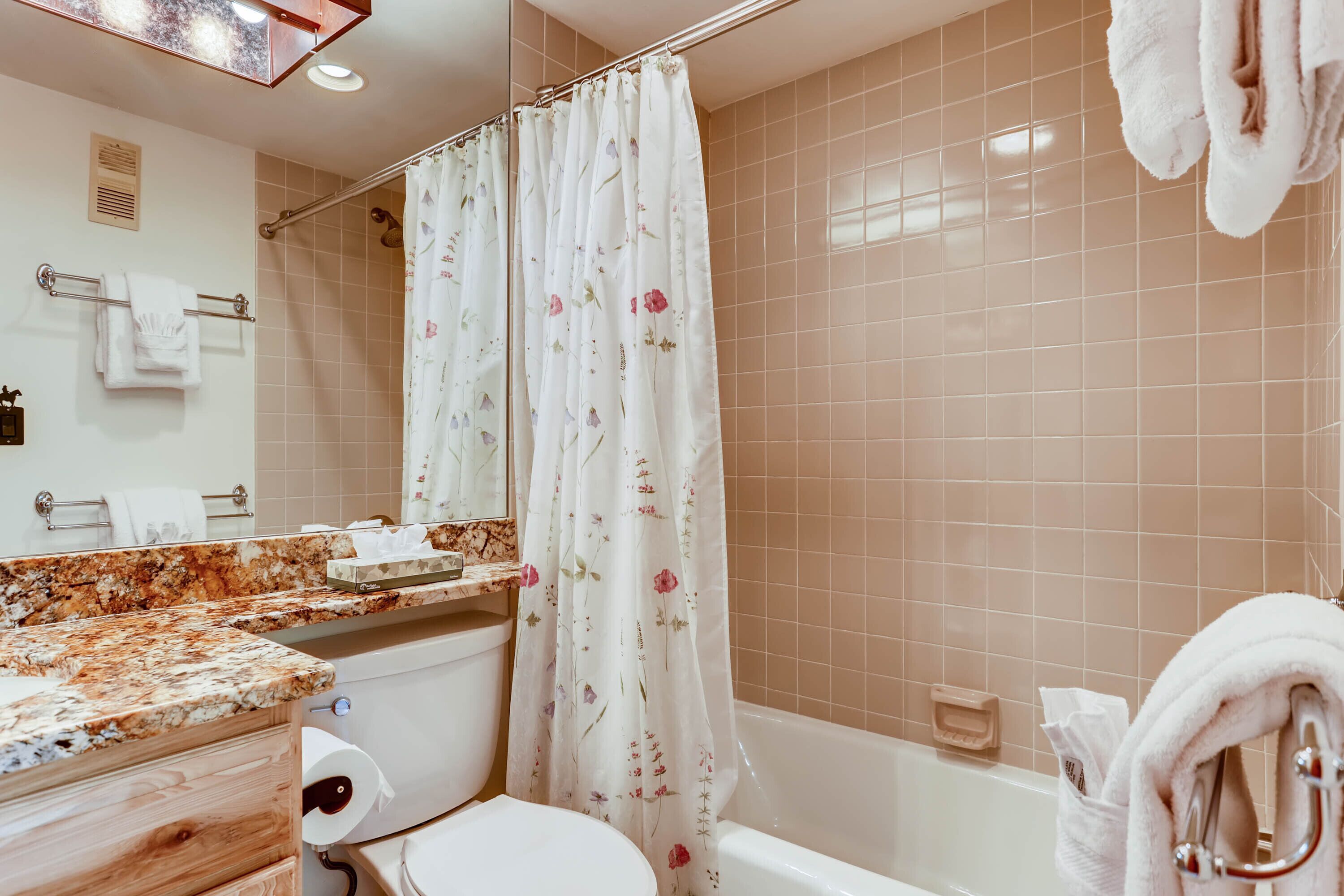 A bathroom with a shower curtain, a toilet, a sink with a marble countertop, and a bathtub.
