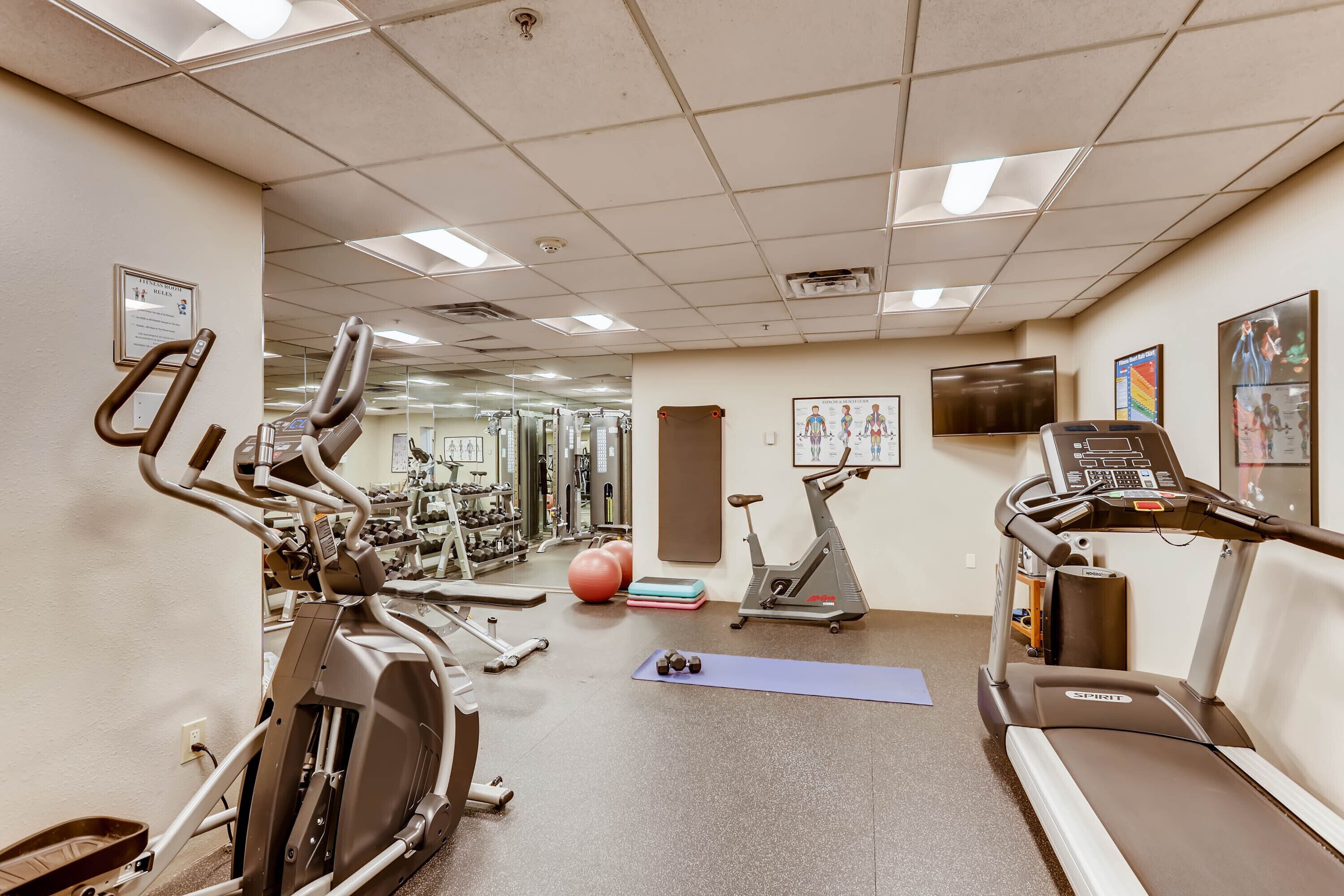 Une salle de sport équipée de divers appareils d’exercice, notamment des tapis de course, des vélos d’appartement et des poids.