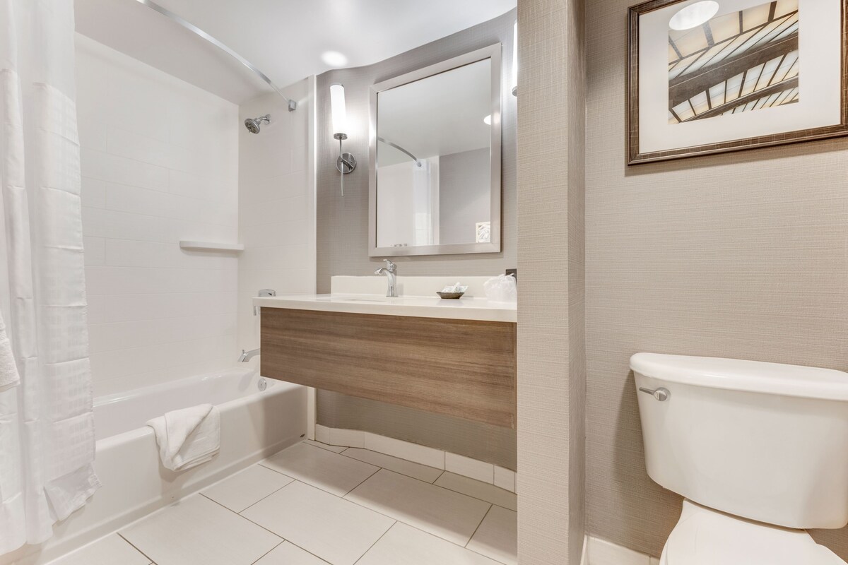 A modern bathroom with a bathtub, a sink with a wooden vanity, a toilet, and a large mirror.