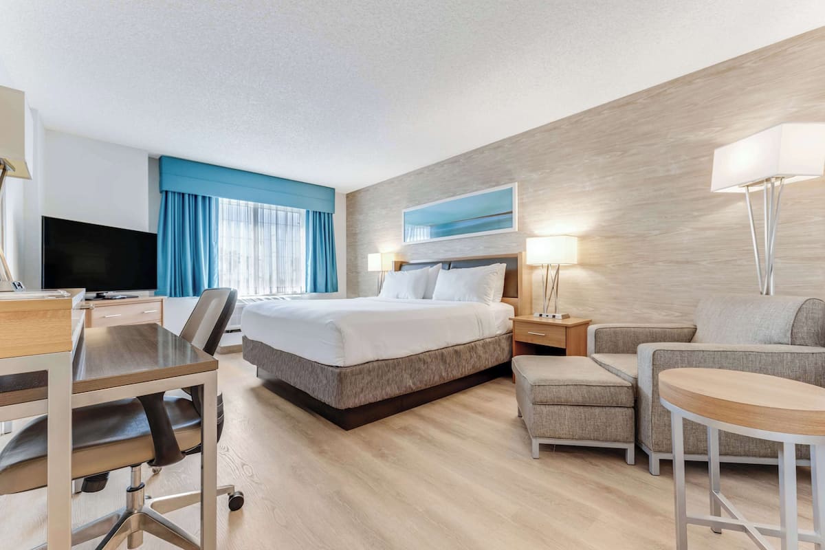 A hotel room with a bed, desk, chair, and a small table.